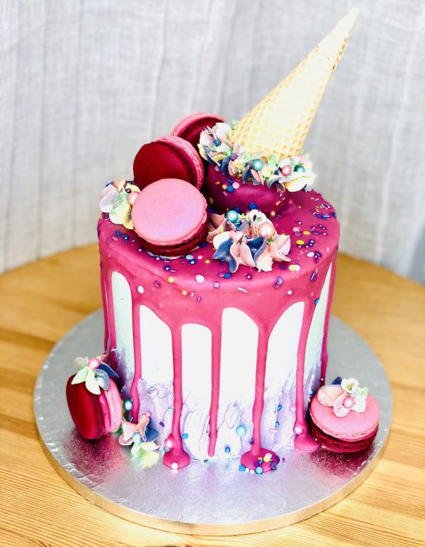 Extravagant luxury pink birthday cake with macarons and ice cream cone topping