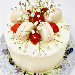 Beautiful gourmet celebration cake topped with fresh French macarons, strawberries and flowers