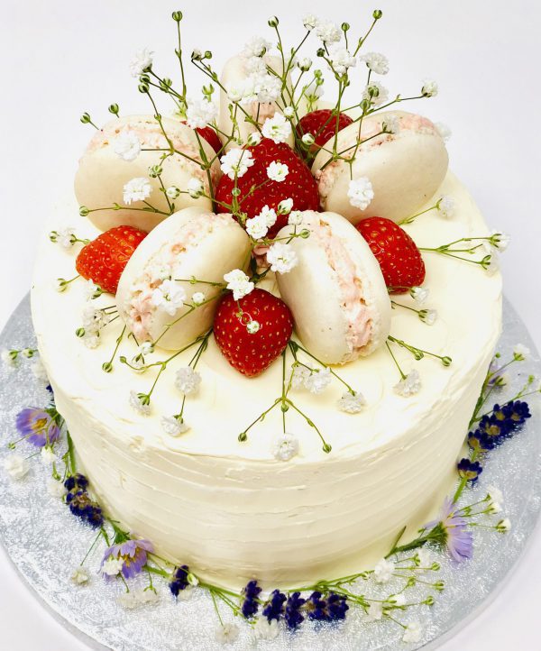 Beautiful gourmet celebration cake topped with fresh French macarons, strawberries and flowers
