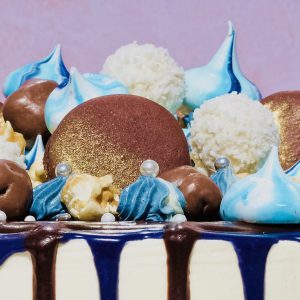 Close up of blue and gold celebration drip cake with blue meringues and macarons