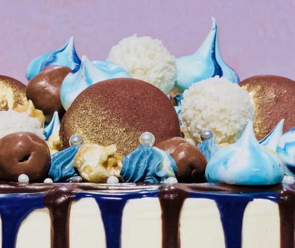 Close up of blue and gold celebration drip cake with blue meringues and macarons