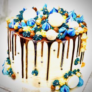 Handcrafted blue and gold ganache drip cake decorated with handmade meringues and macarons