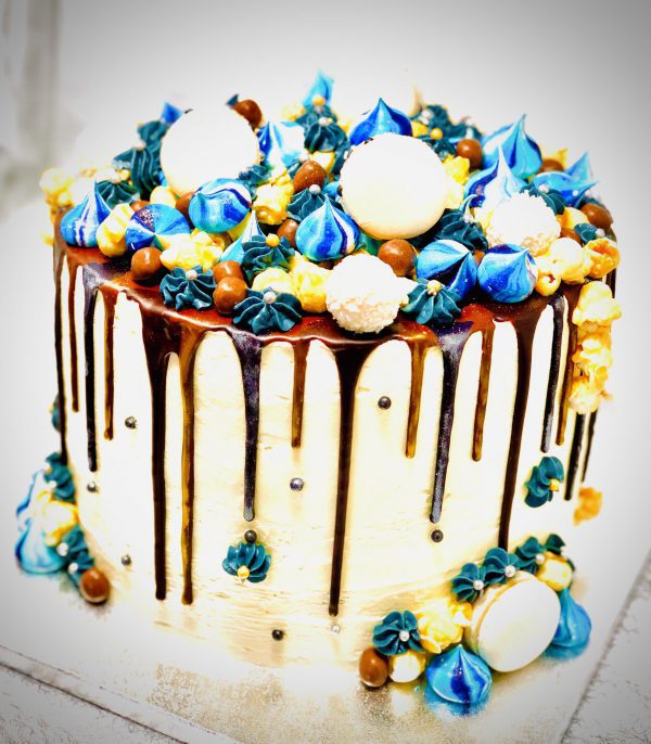 Handcrafted blue and gold ganache drip cake decorated with handmade meringues and macarons