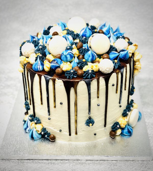 Extravagant gourmet celebration cake with blue and gold ganache drip, macarons and meringues