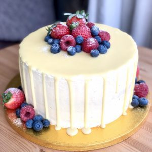 Elegant, freshly baked strawberry and vanilla sponge cake coated in a white ganache drip and berries