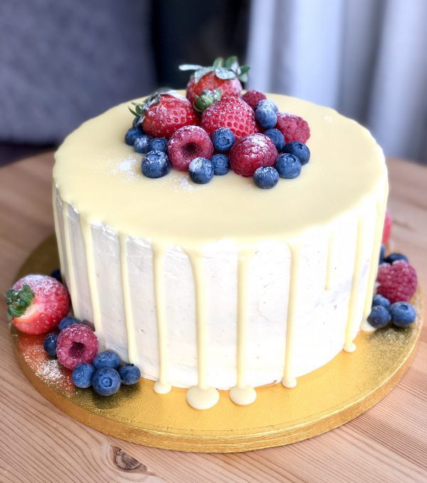 Elegant, freshly baked strawberry and vanilla sponge cake coated in a white ganache drip and berries