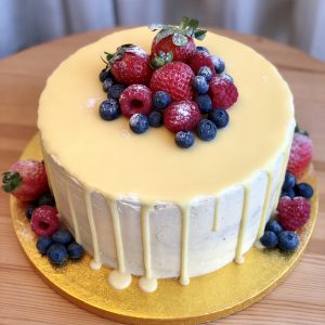 Handcrafted strawberry and vanilla celebration drip cake topped with fresh berries and icing