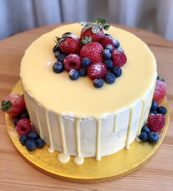 Handcrafted strawberry and vanilla celebration drip cake topped with fresh berries and icing