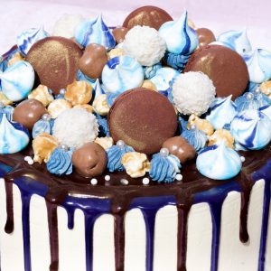 Beautiful blue and gold ganache drip cake topped with blue macarons and meringues