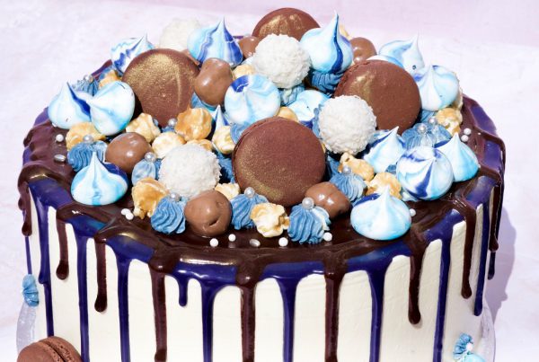 Beautiful blue and gold ganache drip cake topped with blue macarons and meringues