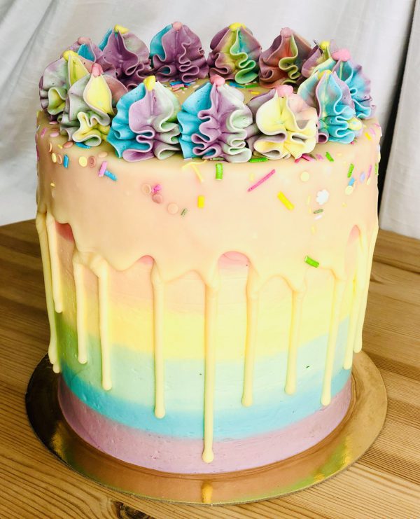 Handcrafted rainbow pinata cake, with colour sprinkles and vanilla drip detail