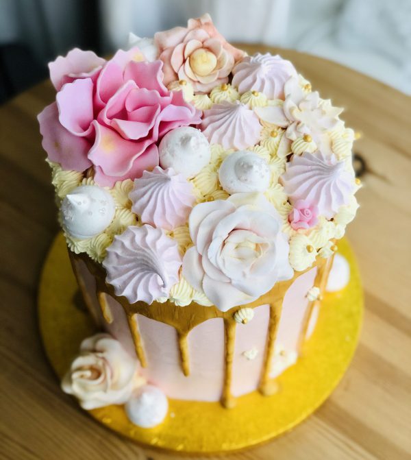 Top of gold drip effect handcrafted cake, decorated with baby pink roses and meringues