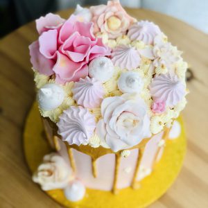 Decoration on top of pink and gold celebration birthday cake with baby pink flowers and buttercream