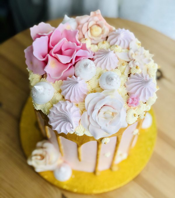 Decoration on top of pink and gold celebration birthday cake with baby pink flowers and buttercream