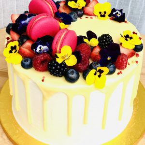 Colourful handcrafted yellow berry cake with pink macarons and yellow flower decoration