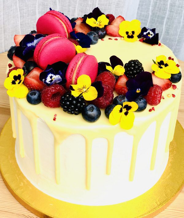 Colourful handcrafted yellow berry cake with pink macarons and yellow flower decoration