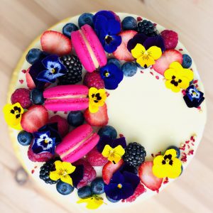 Yellow flower, pink French macaron and berry decoration on handcrafted berry cake