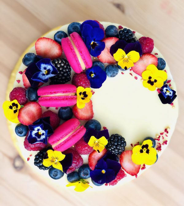 Yellow flower, pink French macaron and berry decoration on handcrafted berry cake