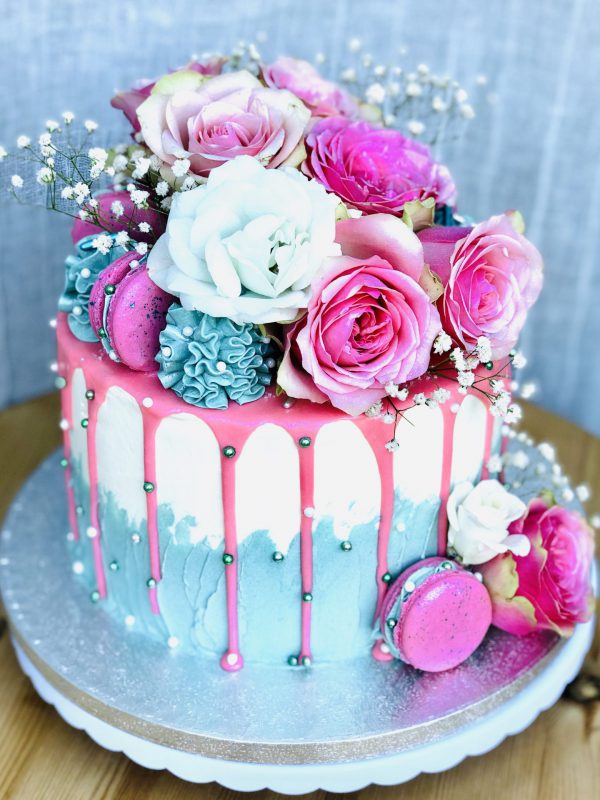 Gourmet pink birthday cake with drip detail with fresh pink and blue flowers and macaron topping