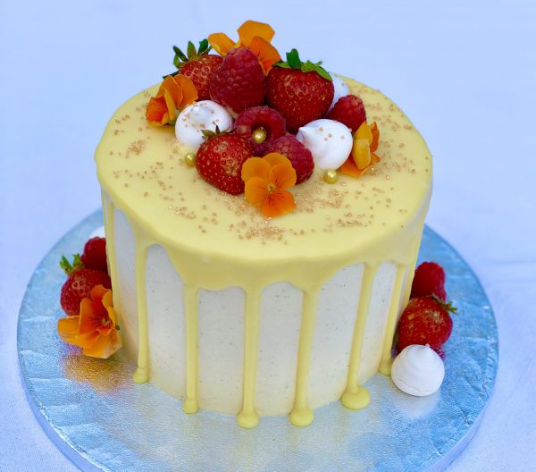 Handcrafted vanilla drip celebration cake with fresh strawberries, raspberries and decorative flowers